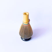 Japanese-made matcha whisk with black, green, and gold thread detailing, crafted from natural bamboo.