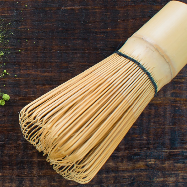 Traditional Japanese bamboo matcha whisk (chasen) on a wooden surface, used for preparing smooth ceremonial grade matcha.