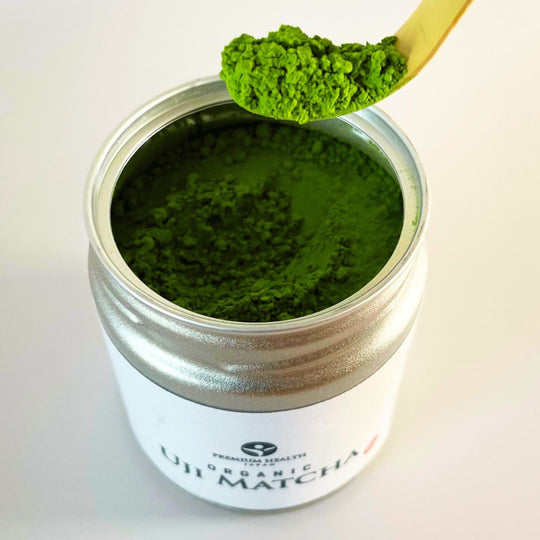 Scoop of vibrant organic Uji matcha powder from Premium Health Japan in a silver tin, ready for traditional tea preparation.
