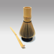 Traditional Japanese matcha whisk placed on black ceramic holder with bamboo chashaku scoop for tea ceremony preparation