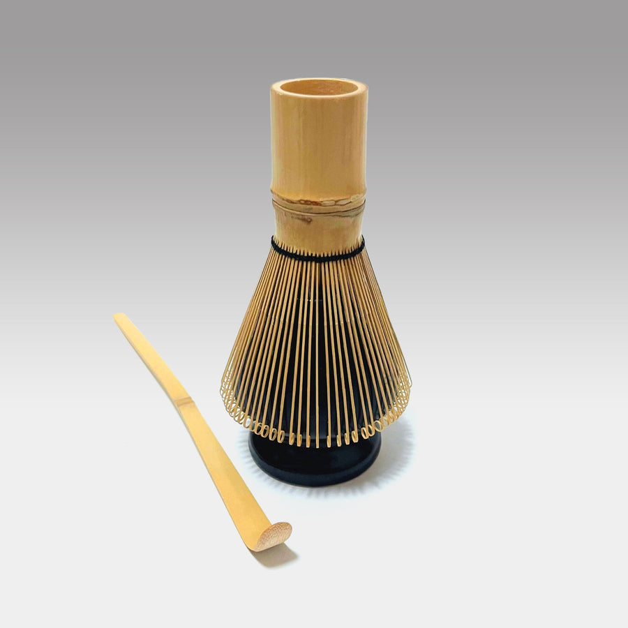 Traditional Japanese matcha whisk placed on black ceramic holder with bamboo chashaku scoop for tea ceremony preparation