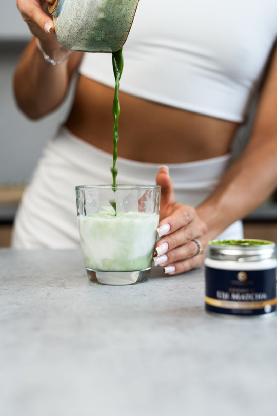 Woman pouring whisked matcha from a chawan into a glass with milk to make a matcha milk tea drink