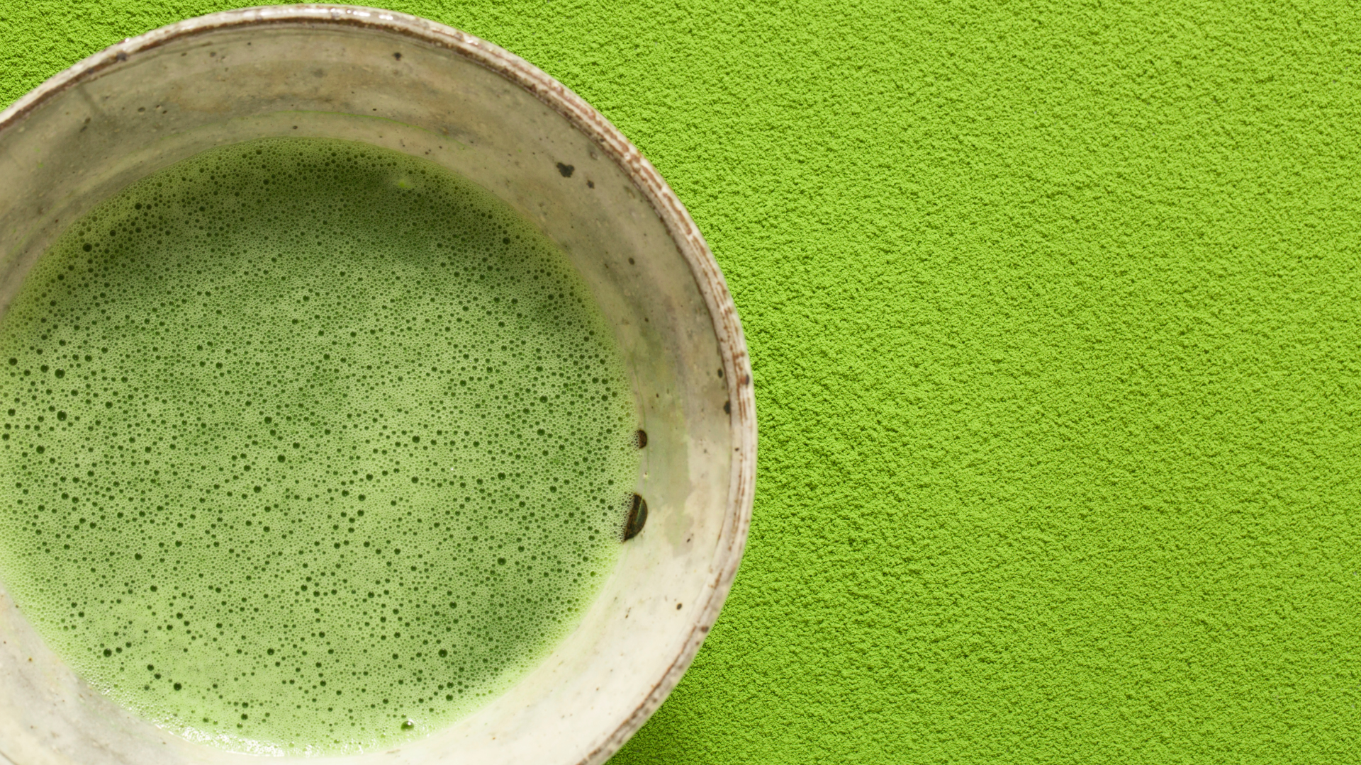 A bowl of matcha green tea on a flat surface covered in matcha powder