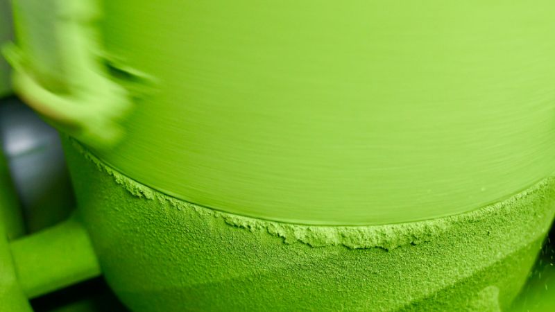 Close-up of a traditional stone mill grinding vibrant green matcha powder in a Japanese tea production facility.