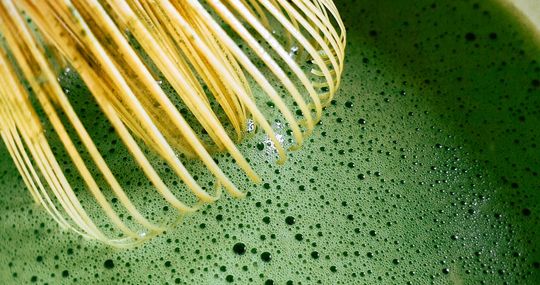 A close-up of matcha tea and it's foam surface with a bamboo chasen whisk