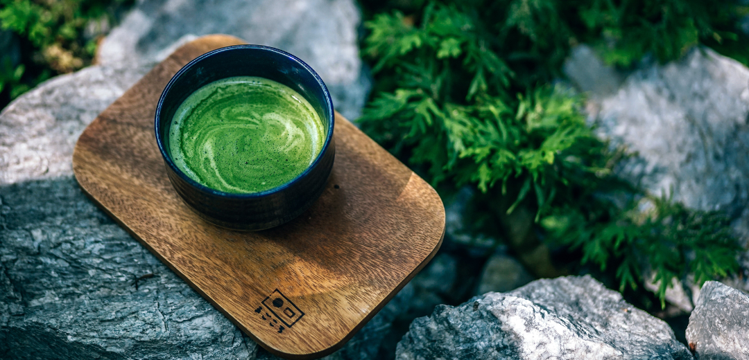 A bowl of matcha tea on a wooden board in a rock garden