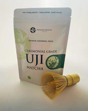 Ceremonial Grade Uji Matcha 100 g pouch with a bamboo chasen placed beside it, photographed in soft natural light.