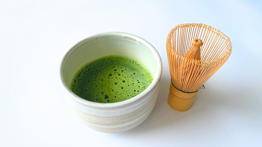 Beige matcha bowl with bright green matcha next to a bamboo whisk