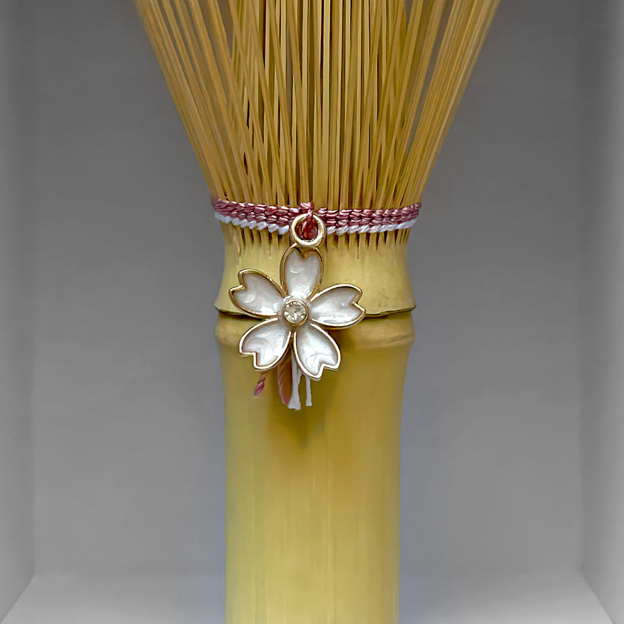 Close-up of pink-threaded matcha whisk handle with sakura charm, handcrafted by Suikaen in Takayama, Japan.