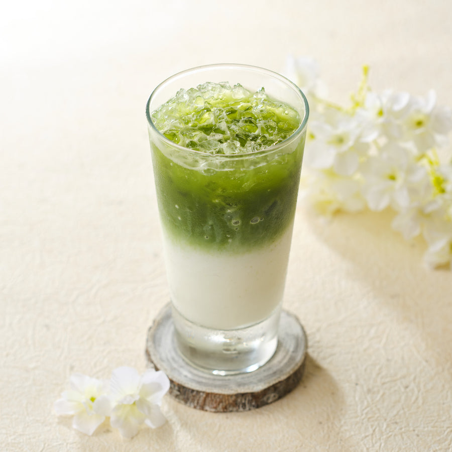 Iced matcha latte with crushed ice made from first spring harvest ceremonial grade Uji matcha, layered green over milk in a tall glass with white flowers