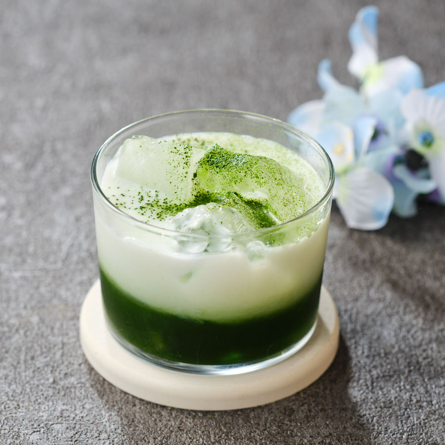 Iced matcha latte made with hand-picked Gokō Samidori Uji matcha, deep green matcha under milk and ice in a short glass, with pale blue flowers behind