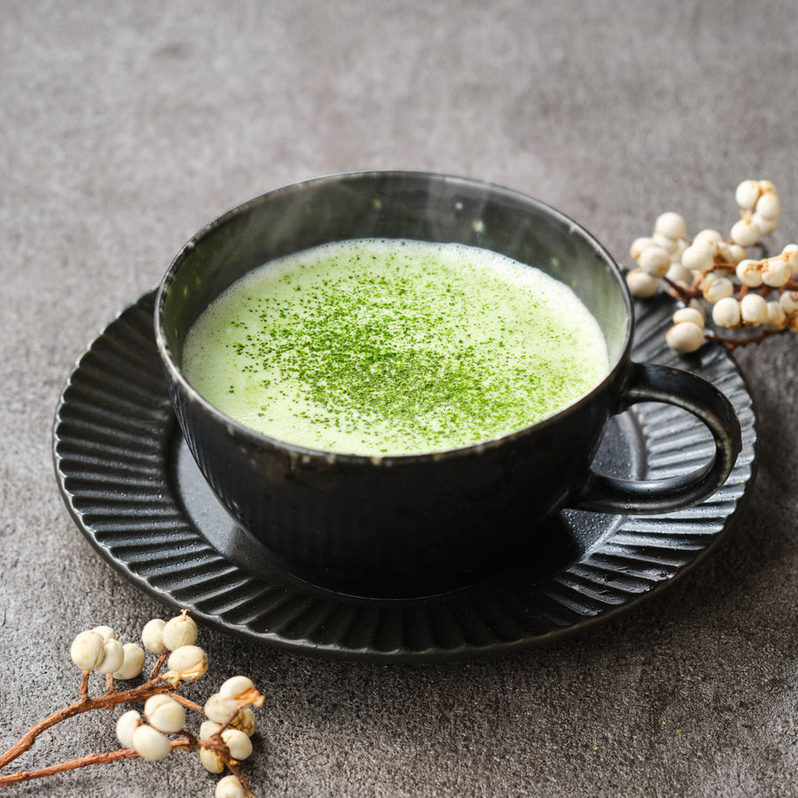 Hot matcha latte made with Uji Matcha Gokō × Samidori blend, matcha dusted over the foam in a black ceramic cup and saucer with white berry branches
