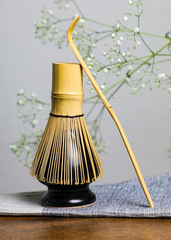 Handcrafted bamboo matcha whisk resting on a black whisk holder with a chashaku beside it, symbolizing traditional Japanese tea ceremony craftsmanship.