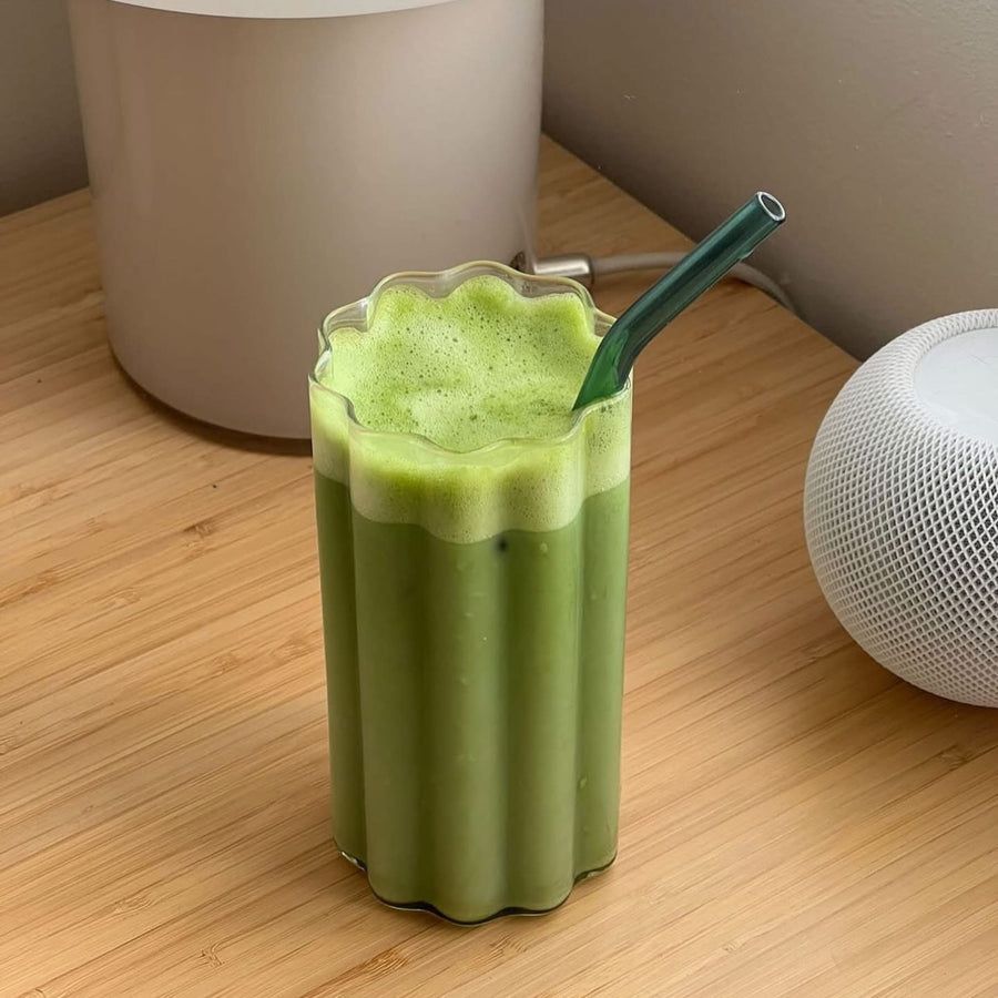 Iced matcha latte in a ripple glass with green straw, served on a wooden table for a modern and refreshing presentation.