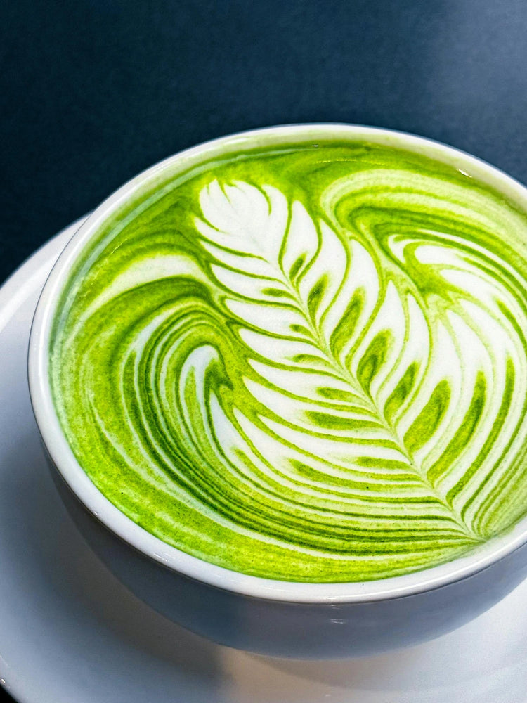 Ceremonial matcha latte with detailed leaf latte art in a white ceramic cup on a clean tabletop