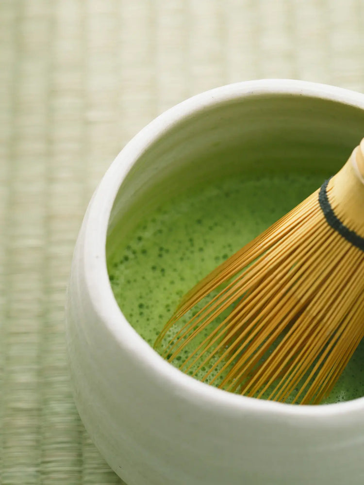 Ceramic matcha tea bowl with freshly whisked green matcha and a bamboo chasen resting inside