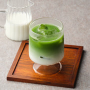 Iced matcha latte made with JAS organic Okumidori matcha, bright green matcha layered over milk and ice in a stemmed glass, with a jug of milk behind