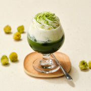 Layered iced matcha with cream and a dusting of matcha in a stemmed glass on a wooden coaster