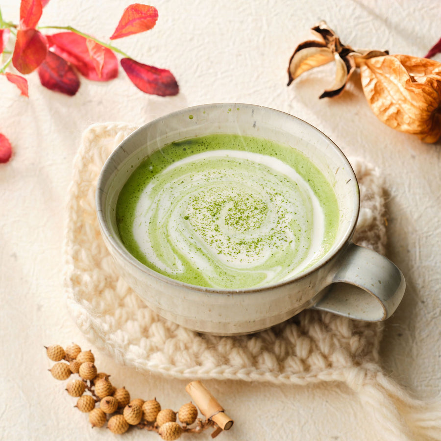 Matcha latte in a ceramic mug on a knit cloth with autumn leaves and dried flowers
