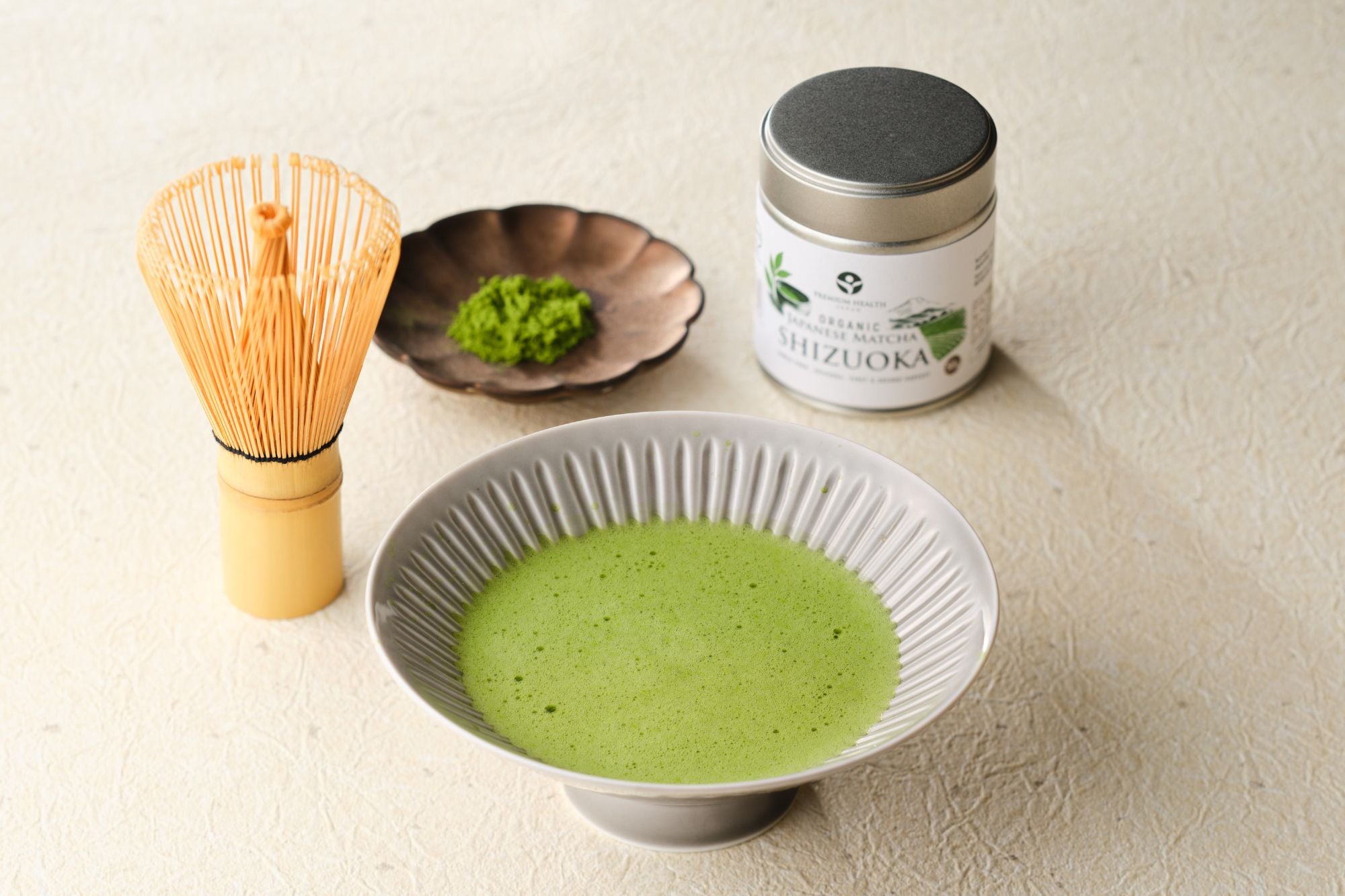 Bowl of freshly whisked usucha with a bamboo chasen, dish of matcha powder, and the Organic Japanese Matcha Shizuoka tin
