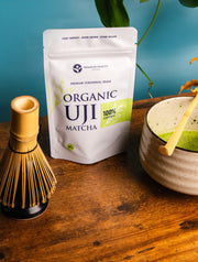 Organic Uji Matcha 40g ceremonial grade pouch with whisk and matcha bowl on wooden table, Premium Health Japan product photo.