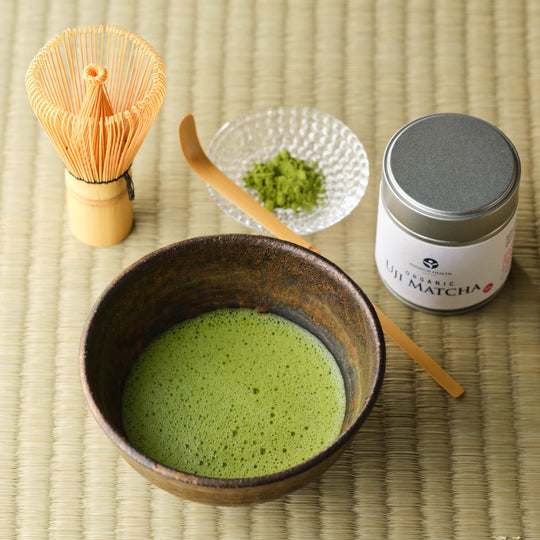 Organic Uji Matcha Ceremonial Grade Classic Blend 50g tin with bamboo chasen whisk, chashaku scoop, matcha powder in a glass dish and a whisked bowl on tatami