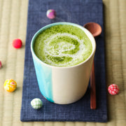 Steaming hot matcha latte made with Organic Uji Matcha Classic Blend, with a swirl of matcha dusted on the milk foam in a turquoise ceramic cup