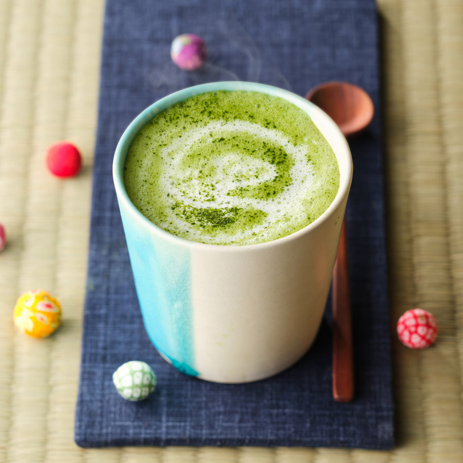 Steaming hot matcha latte made with Organic Uji Matcha Classic Blend, with a swirl of matcha dusted on the milk foam in a turquoise ceramic cup