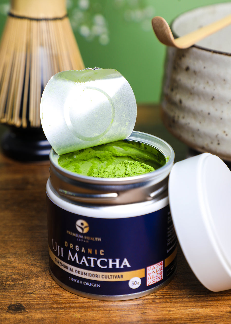 Opened tin of Organic Uji Matcha Okumidori cultivar 30g showing vibrant green powder beside bamboo whisk and chawan, representing Kyoto’s matcha tradition.