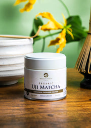 Organic Uji Matcha Saemidori cultivar in a 30g ceremonial tin with whisk and matcha bowl on a wooden table