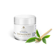 Organic Uji Matcha Saemidori 30 g jar with white label, beside a bamboo chashaku spoon of bright green matcha powder and fresh tea leaves
