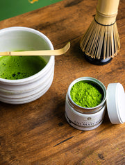 Organic Uji Matcha Saemidori cultivar in an open 40g tin beside a matcha bowl and bamboo whisk.