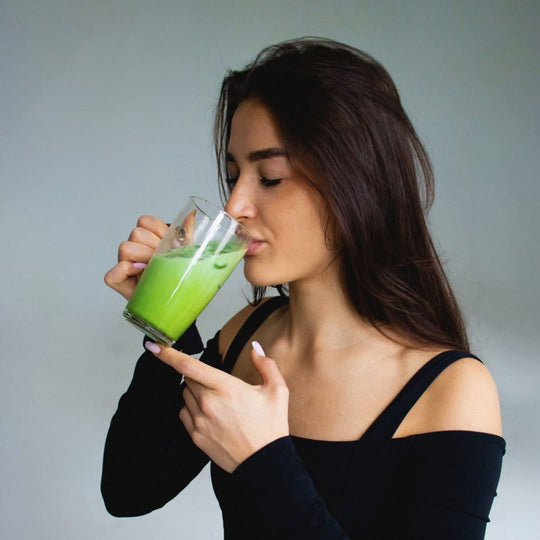 Woman in a black top enjoying an iced organic Uji matcha latte from a clear glass, highlighting vibrant green color.