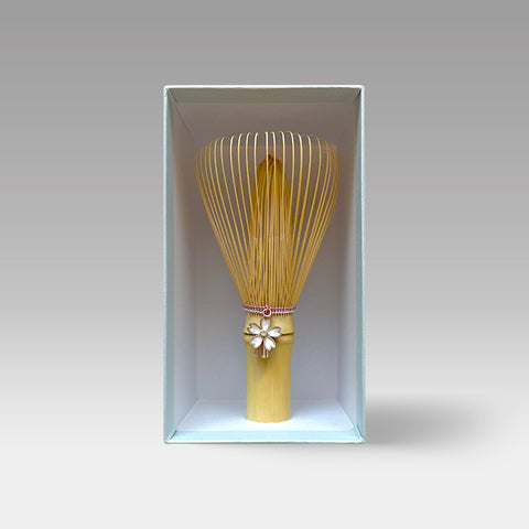 Japanese matcha whisk with pink thread and sakura charm, handcrafted by Suikaen in Takayama, displayed in box.