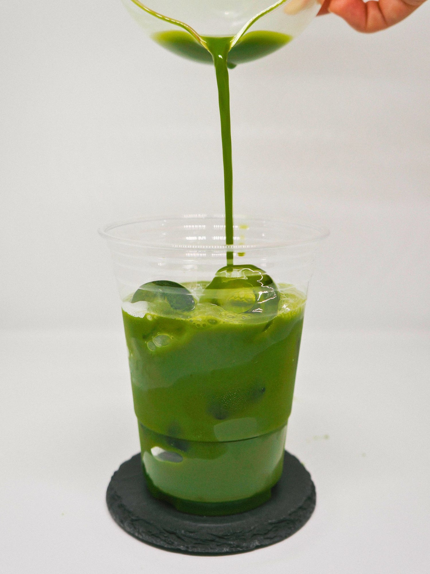 Iced matcha latte being poured from a glass bowl into a clear cup, showcasing vibrant green color and smooth texture.