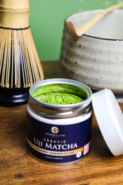 Premium Health Japan Ceremonial Organic Uji Matcha Okumidori cultivar 30g tin opened beside bamboo whisk and chawan, showcasing Kyoto’s tea culture.
