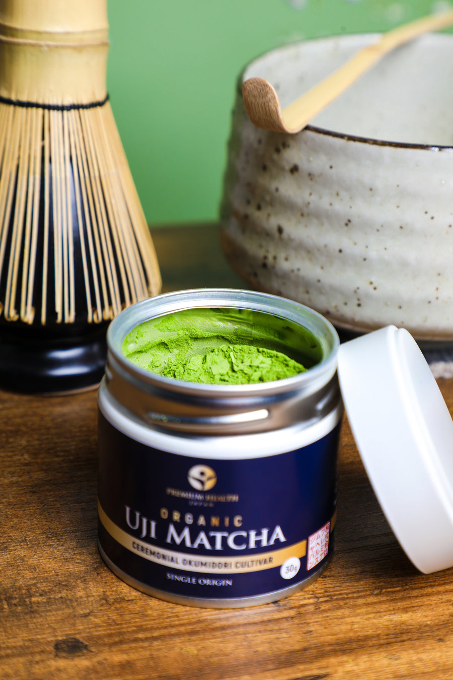 Premium Health Japan Ceremonial Organic Uji Matcha Okumidori cultivar 30g tin opened beside bamboo whisk and chawan, showcasing Kyoto’s tea culture.