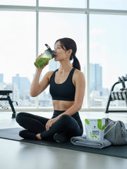 Woman in black activewear drinking a matcha shake at the gym, with Premium Health Japan 100% Organic Japanese Matcha 50g pouch beside her.
