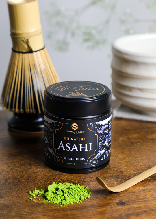 Premium Health Japan Uji Matcha Asahi 30g tin from the Signature Uji Series with bamboo whisk, chashaku, and matcha powder on wooden table in Kyoto setting.