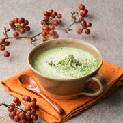 Hot Saemidori matcha latte topped with whipped cream and dusted matcha, in a brown stoneware cup with a wooden spoon and red berry branches