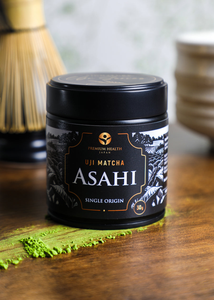 Uji Matcha Asahi single-origin 30g tin on a wooden surface with matcha powder and bamboo whisk in background, highlighting authentic Kyoto craftsmanship.