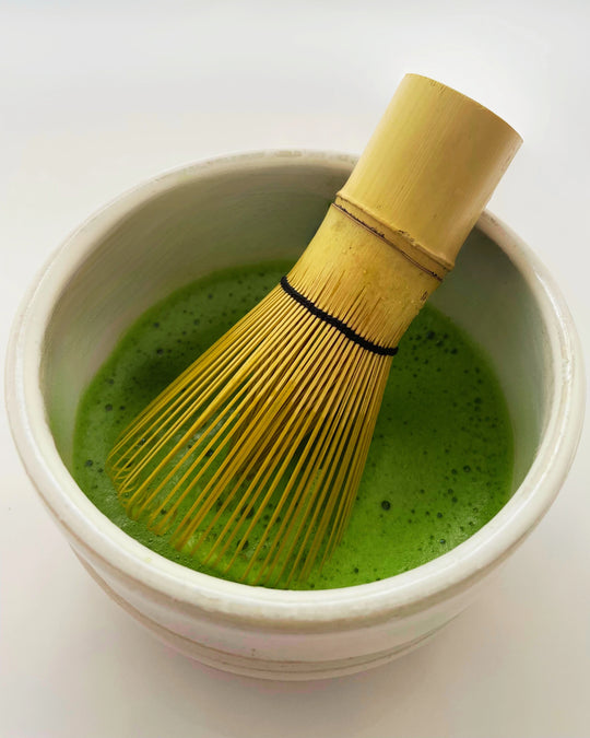 Ceremonial grade Uji matcha whisked in a chawan with a bamboo chasen, showing a smooth vibrant green foam.