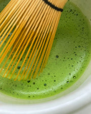 Close-up of vibrant ceremonial grade Uji matcha being whisked with a bamboo chasen, showing smooth foam and bright green colour.