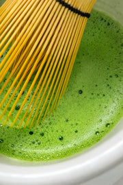 Close-up of vibrant ceremonial grade Uji matcha being whisked with a bamboo chasen, showing smooth foam and bright green colour.