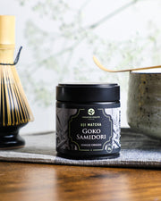 Premium Health Japan Uji Matcha Gokō Samidori 30g single-origin tin placed on a cloth beside a chawan and bamboo whisk, representing Kyoto matcha tradition.