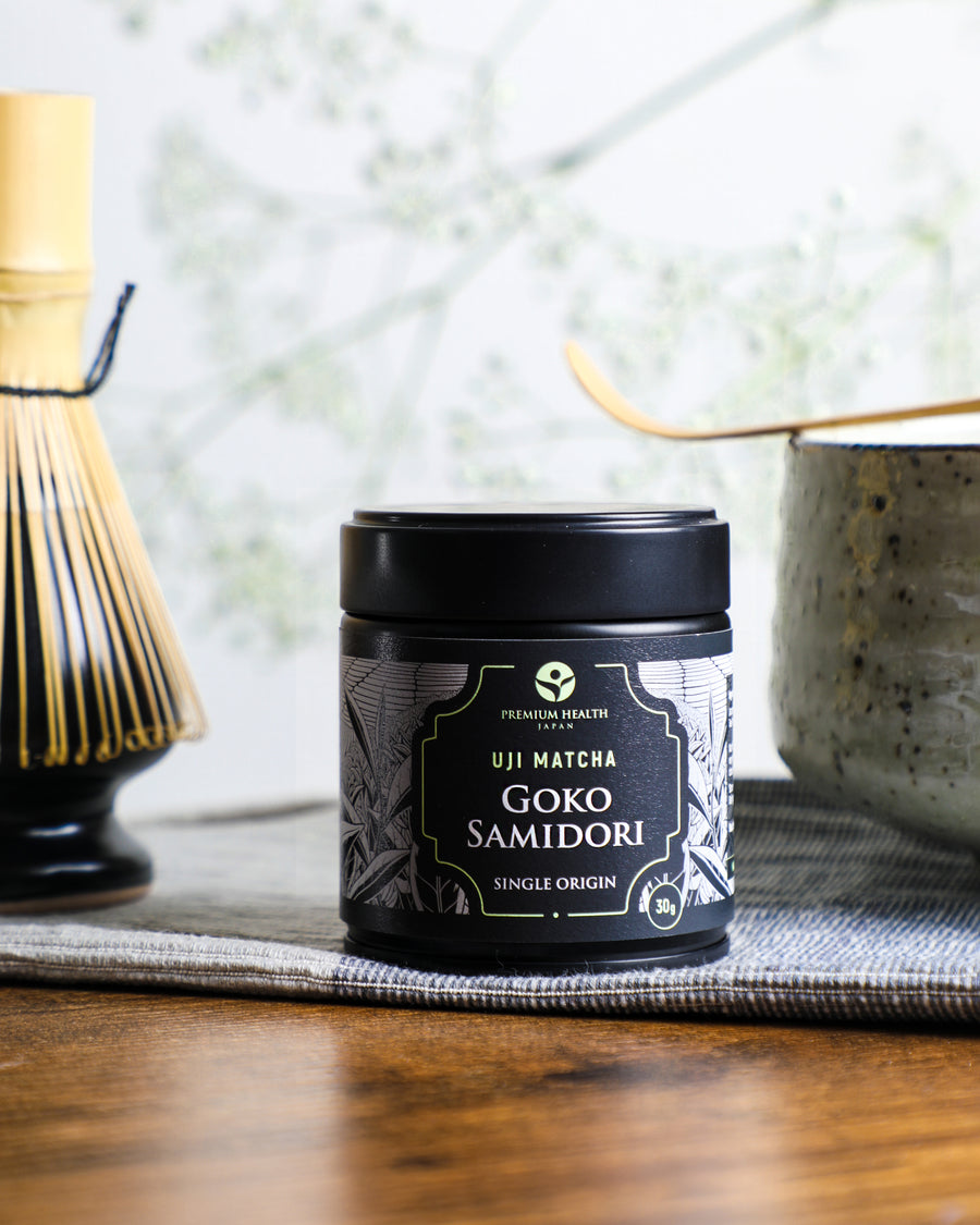 Premium Health Japan Uji Matcha Gokō Samidori 30g single-origin tin placed on a cloth beside a chawan and bamboo whisk, representing Kyoto matcha tradition.