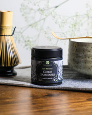 Premium Health Japan Uji Matcha Gokō Samidori 30g tin beside a bamboo whisk and chawan, showcasing authentic single-origin Kyoto matcha preparation.