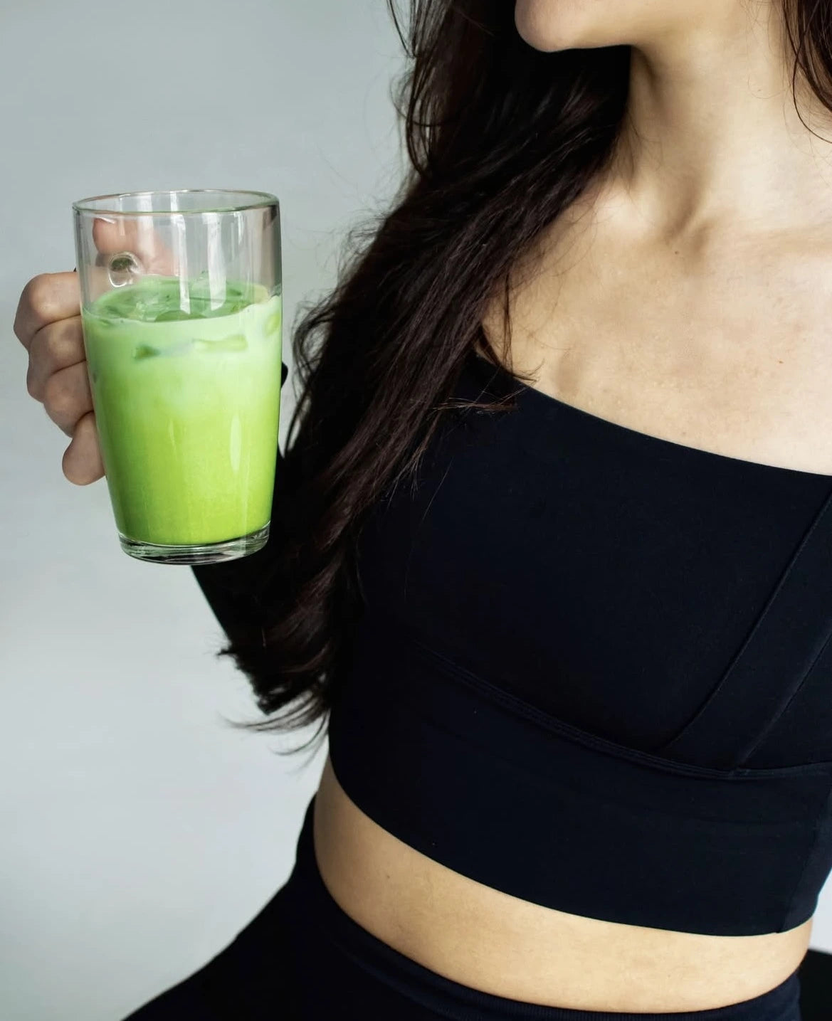 Person holding a glass of iced matcha latte in a bright setting.