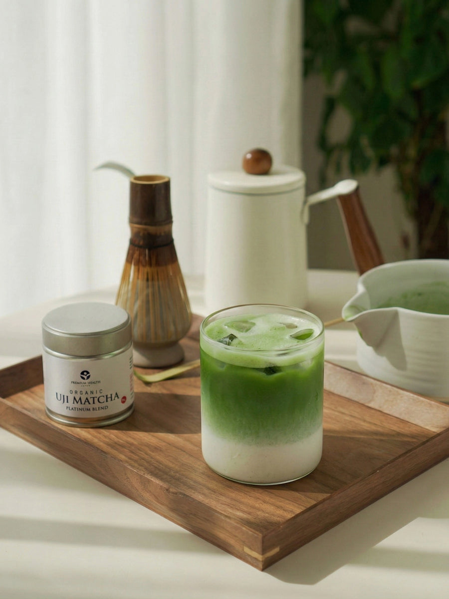 Iced Uji matcha latte with Premium Health Japan Platinum Blend matcha and bamboo whisk on wooden tray