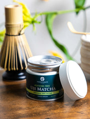 Pesticide-free Uji Matcha Gokō cultivar tin opened on a wooden table with chasen and matcha tools in the background
